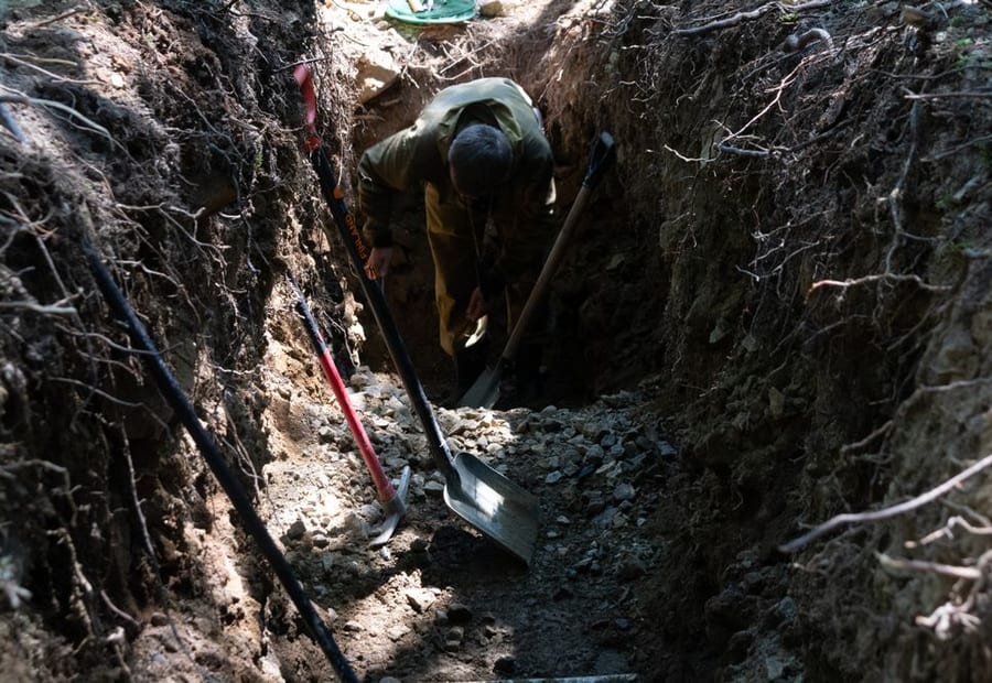 Soil profile exposed in a backhoe test pit showing thin soil over dolomite bedrock on an Olmsted County lot